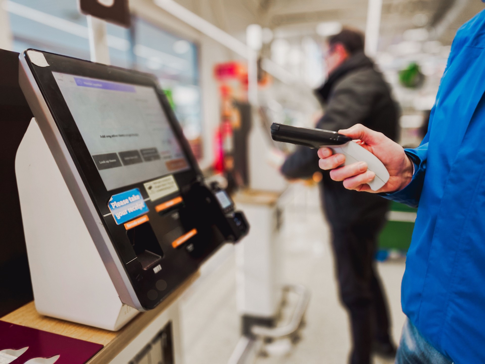 Man holding bar code scanner at self-checkout in store